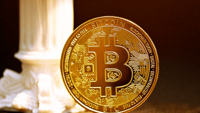 Gold Bitcoin coin standing beside a white classical column