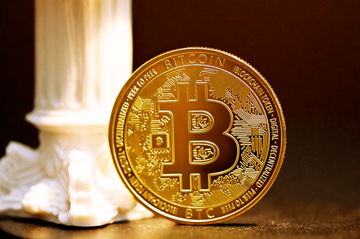 Gold Bitcoin coin standing beside a white classical column