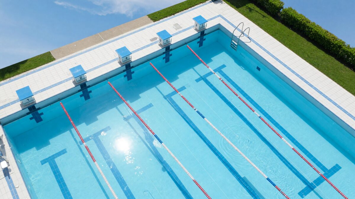 A bright outdoor public swimming pool with lane lines and starting blocks in clear daylight