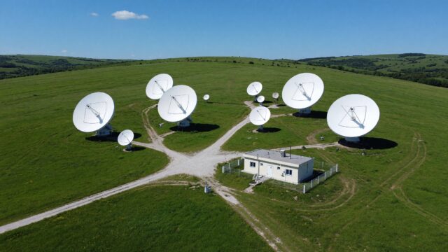 Aerial view of a satellite ground station with white dish antennas on a green plateau under a clear blue sky