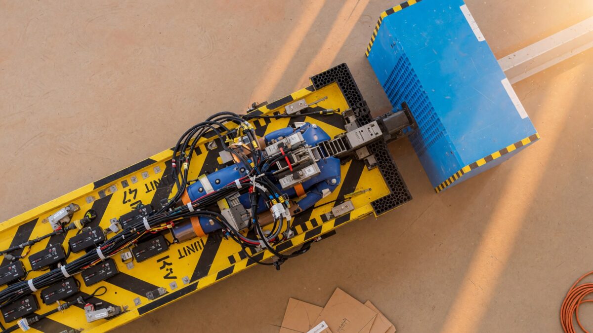 An instrumented yellow and black crash-test sled with cable harnesses an instant before a bright blue impact barrier in a clean laboratory